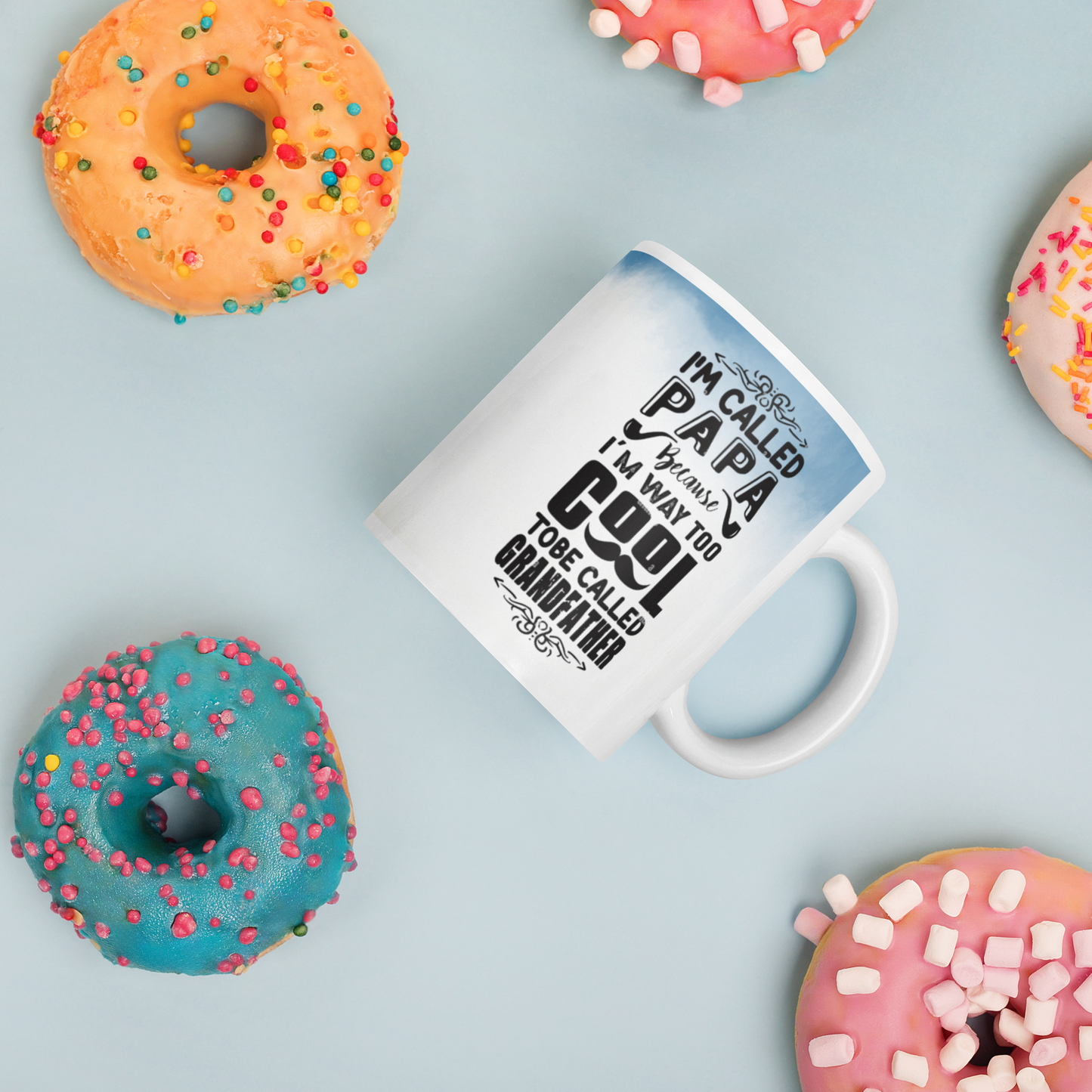 White ceramic mug with text 'I'm called Papa' surrounded by colorful donuts on a light blue background.