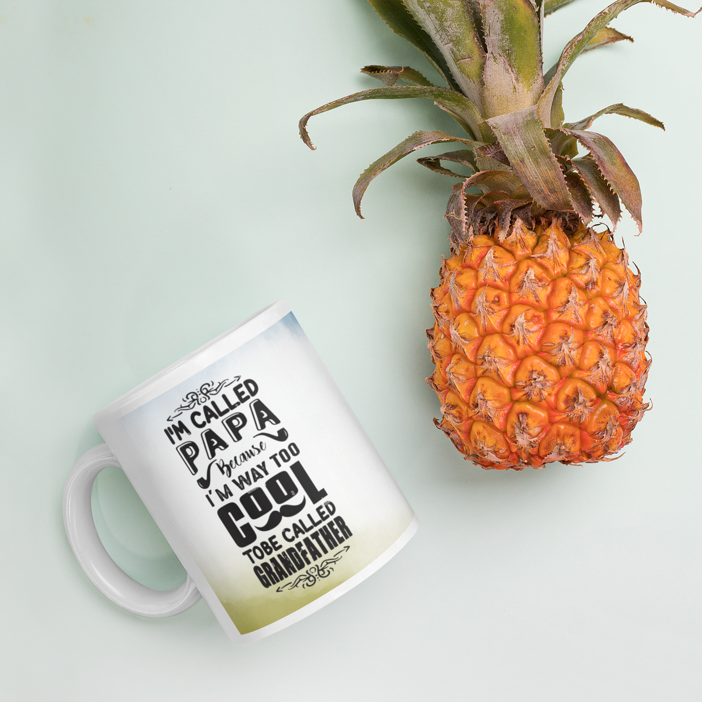 Ceramic mug with the text 'I'm called Papa, I'm way too cool to be called Grandfather' beside a fresh pineapple.