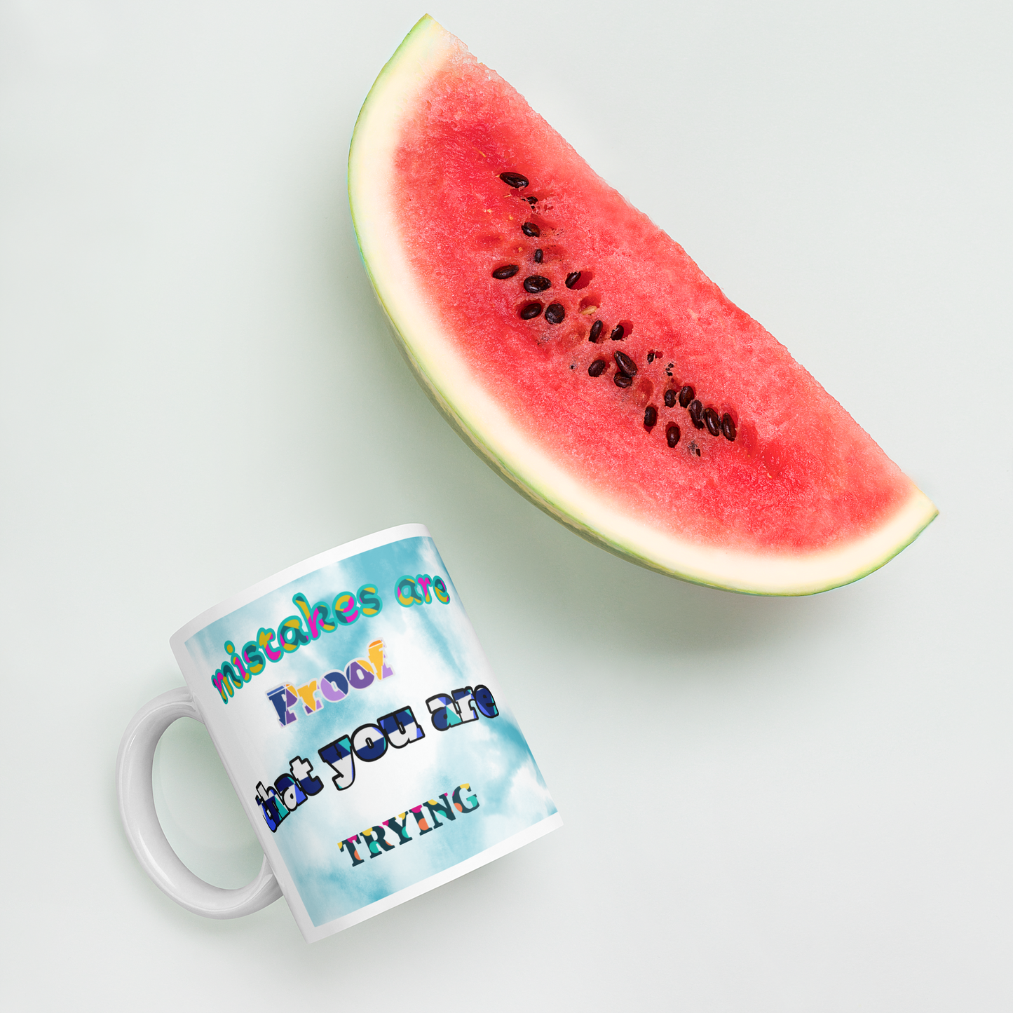 Colorful ceramic mug with motivational text next to fresh watermelon, perfect for coffee or tea lovers.