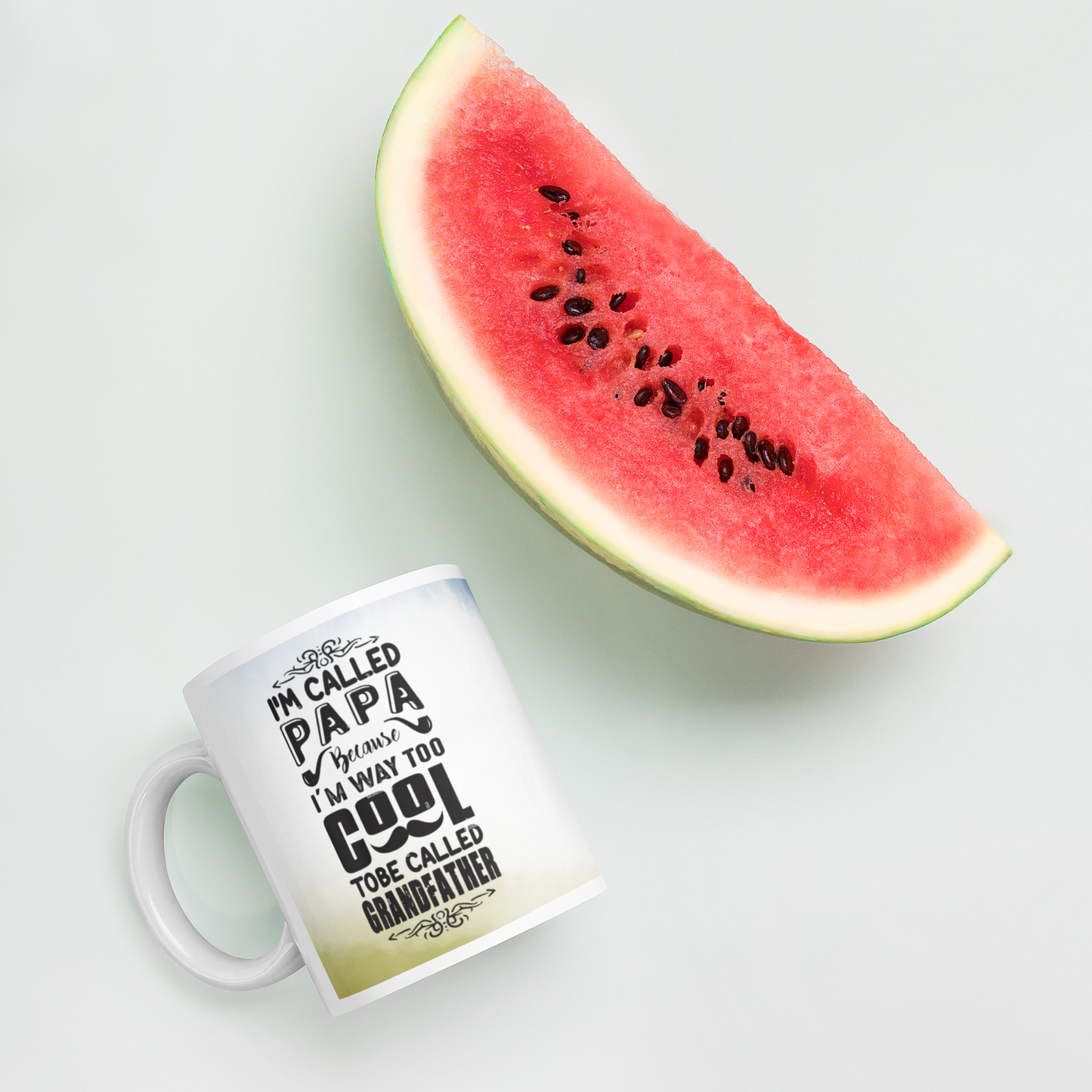 Ceramic mug with text 'I'm called Papa, I'm way too cool to be called Grandfather' next to a slice of watermelon.