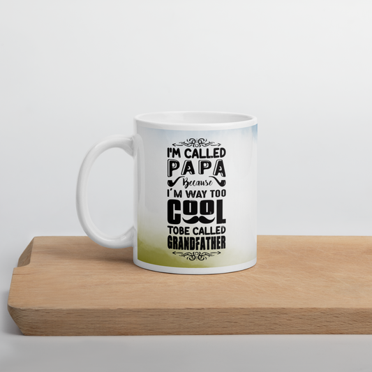 White ceramic mug with text 'I'm called Papa because I'm way too cool to be called Grandfather' on wooden surface.