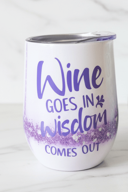 Stemless wine tumbler with purple marble design and glitter base, featuring 'Wine Goes In, Wisdom Comes Out'.